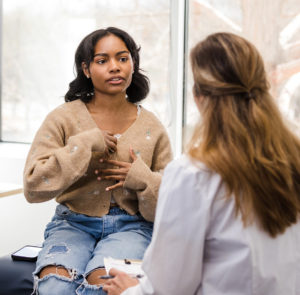 Young woman explains symptoms to unrecognizable female doctor